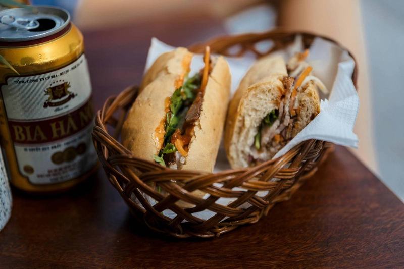 Vietnamese bánh mì sandwich with cilantro, pork, and chili sauce next to a Bia Hà Nội can
