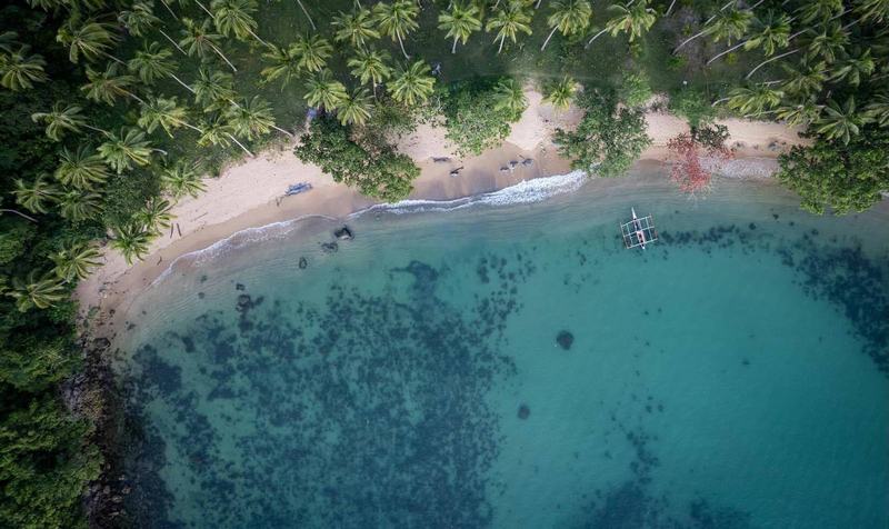 Aerial view of Bebeladan Beach in El Nido, Palawan with palm trees, sandy shore, and turquoise reef-streaked water