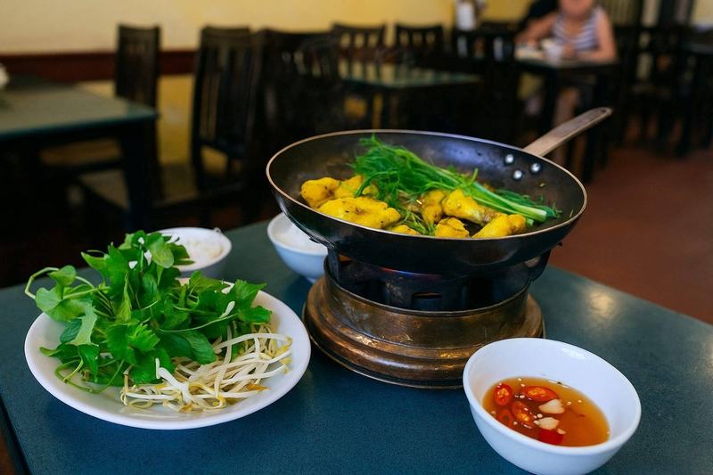 Hanoi-style chả cá sizzling in a pan with turmeric, dill, and green onions