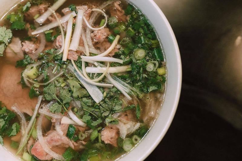 Close-up of Hanoi-style phở with herbs, beef, and scallions in hot broth