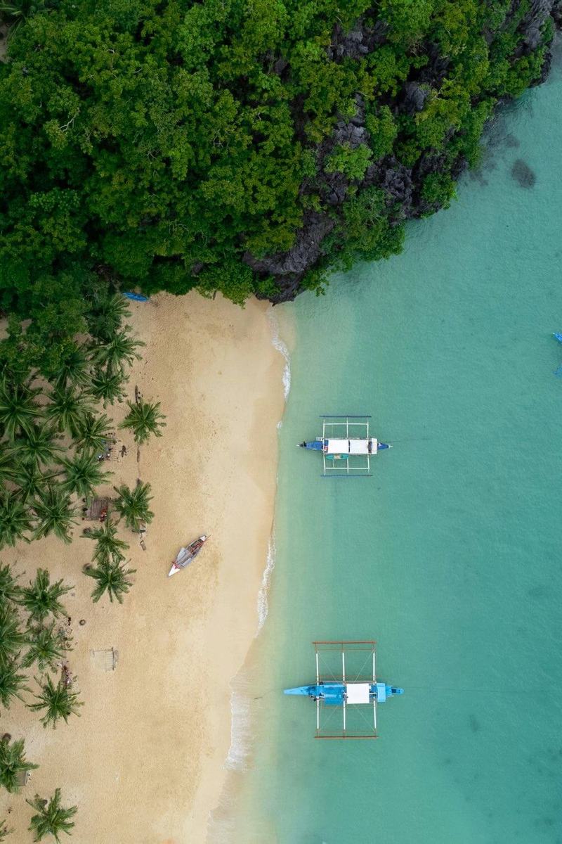 Aerial view of Seven Commandos Beach in El Nido, Palawan with white sand, turquoise water, and palm trees